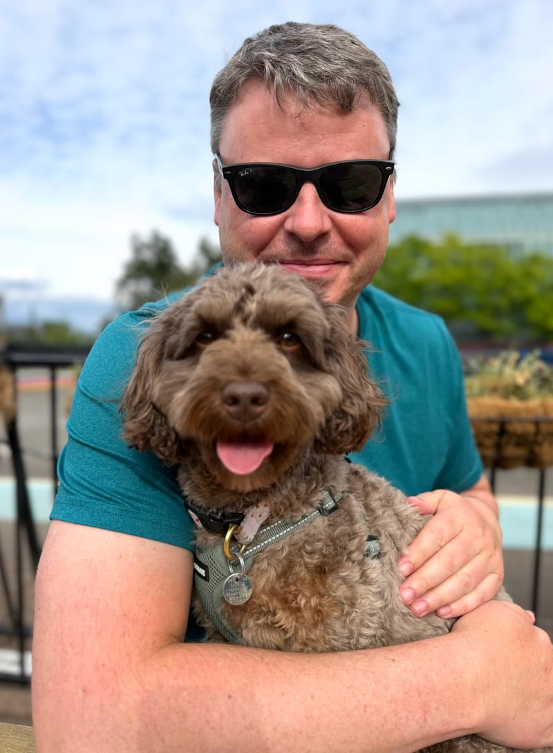 Steve outdoors in sunglasses, holding Luca, who is looking at the camera.